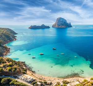 T&uuml;rkisfarbene Bucht mit Es Vedr&agrave; bei Ibiza, umgeben von Booten und Felsk&uuml;ste.