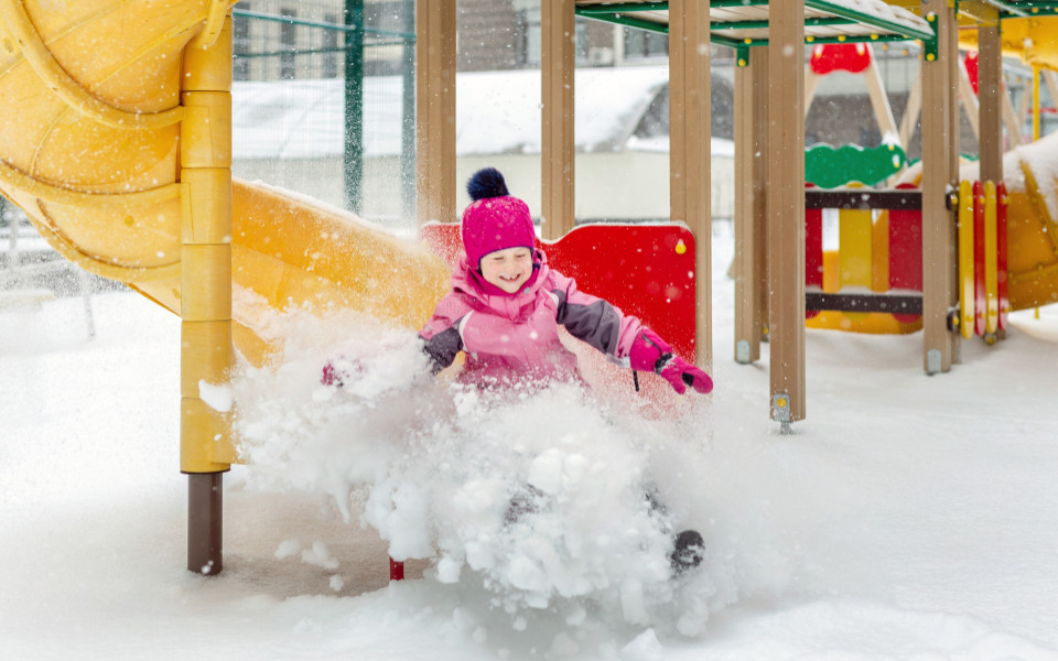 Kleines M&auml;dchen mit pinker M&uuml;tze und Winterjacke, das sich im Winter auf dem Spielplatz vergn&uuml;gt.