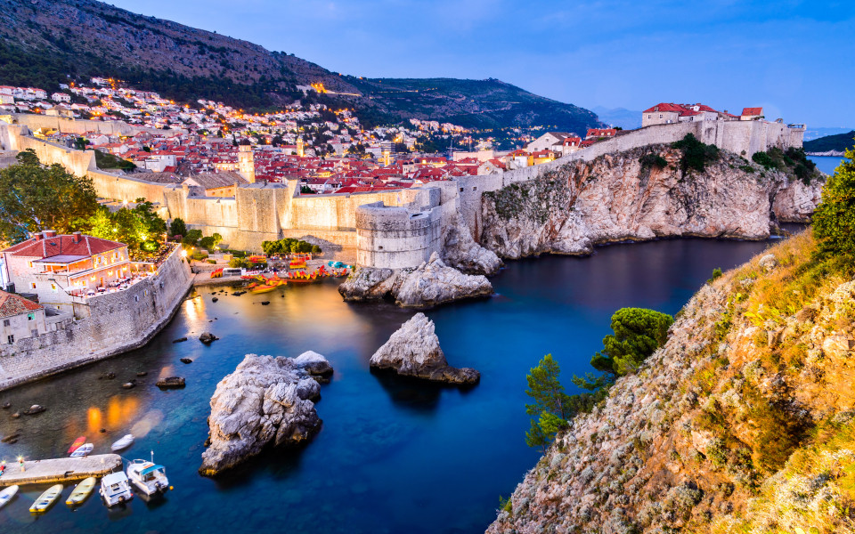 Blick auf die Altstadt von Dubrovnik mit ihren mittelalterlichen Stadtmauern und dem t&uuml;rkisblauen Wasser im Vordergrund.