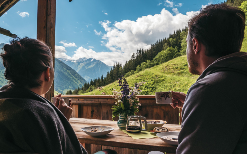 Zwei Personen sitzen auf einer Terrasse, genie&szlig;en Kaffee und Geb&auml;ck, w&auml;hrend sie auf die Berge des Berchtesgadener Landes blicken.